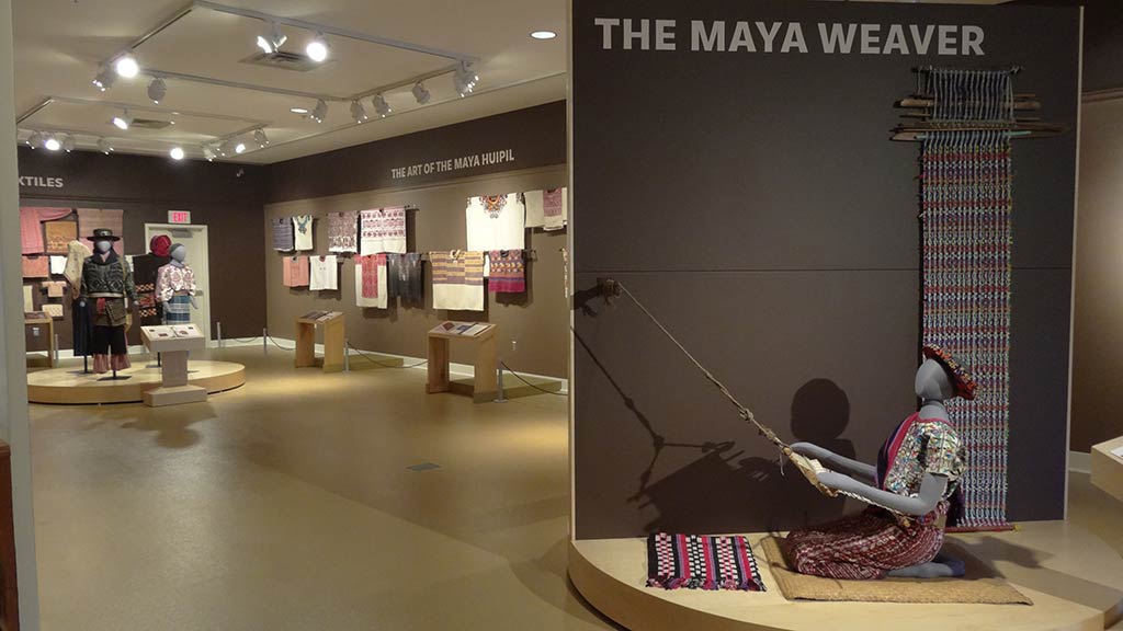 a dressed weaver at work with the rest of the exhibit in the background