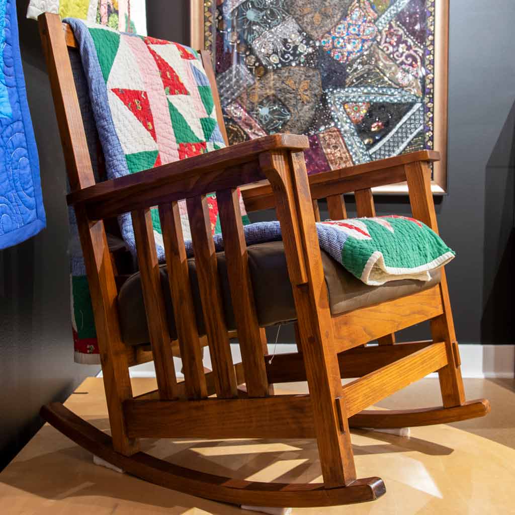 A wooden rocking chair with a green, white, blue, and red quilt