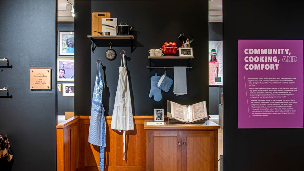 An overview of community, cooking, and comfort section of the exhibit, displaying aprons, mittens, and cooking supplies