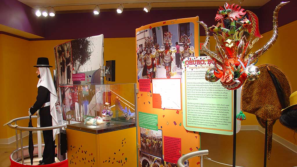side view gallery view featuring a man dressed in carnival clothing and the dragon sculpture with associated text
