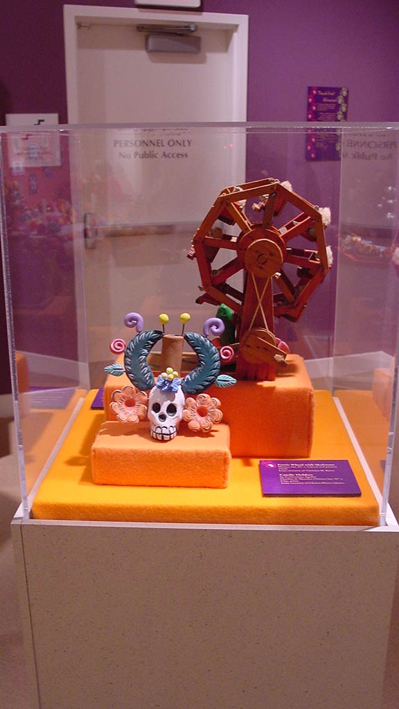 opposite side of display case with skeleton wearing a headpiece in front of the skywheel made of wood
