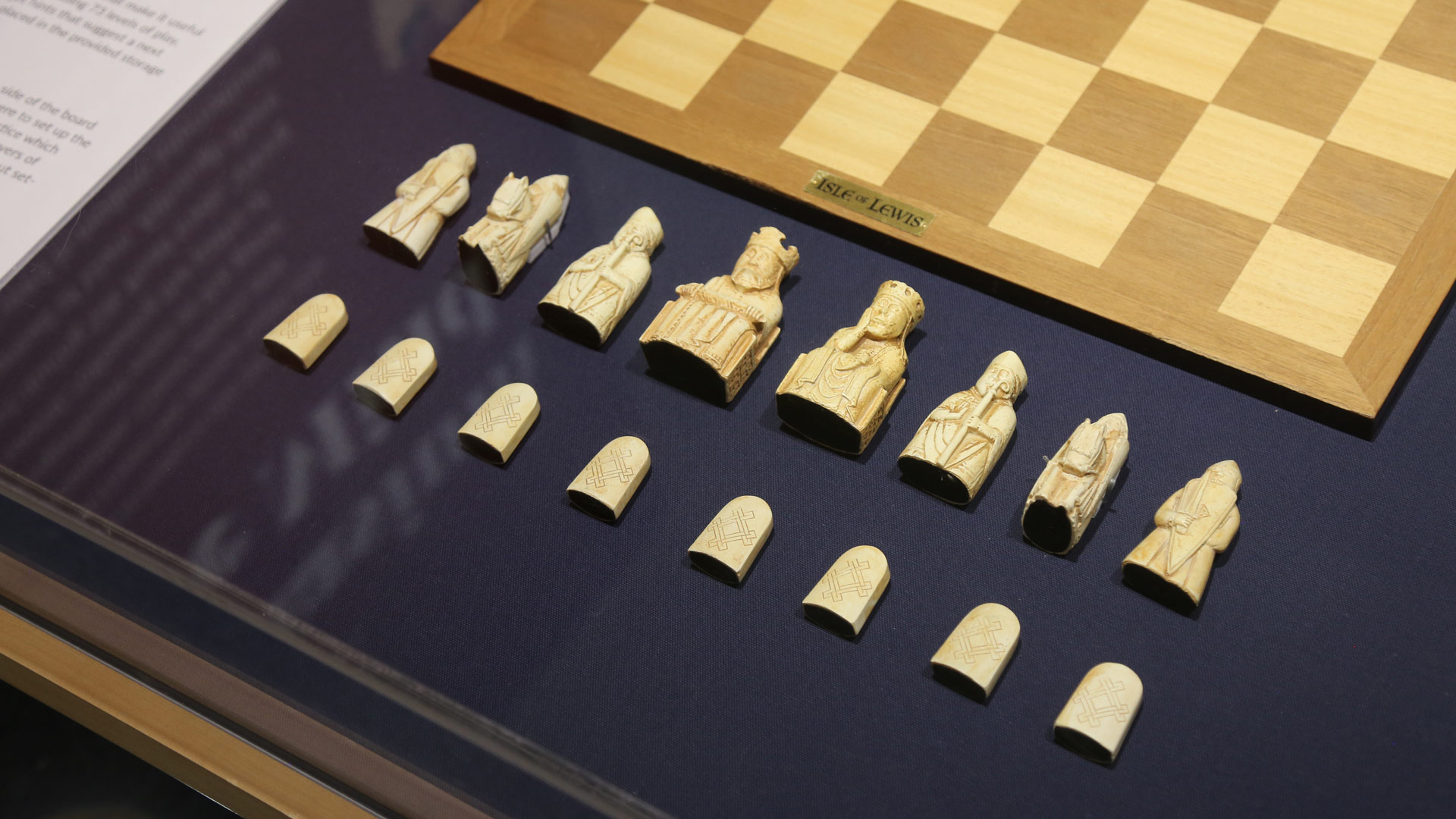 closeup shot of chess pieces from the first display case, in front of a chessboard titled 'isle of lewis'
