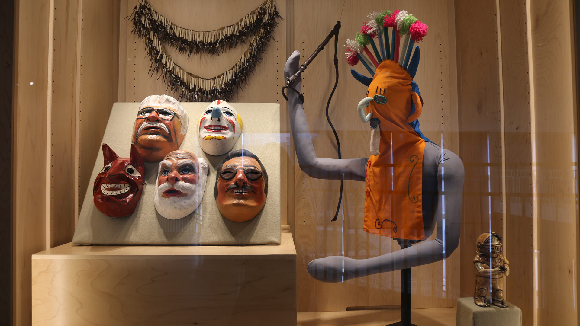 front view of the exhibit case with the shoulder sling, masks, mannequin with a whip, and football player sculpture