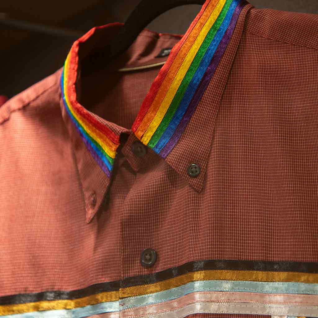 A close up of a brown shirt's collar with rainbow ribbon