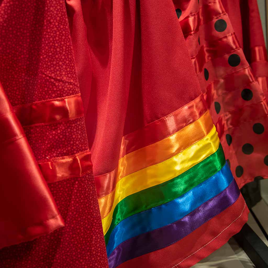 A close up view of a red skirt with red ribbon, a red skirt with rainbow ribbon, and a red skirt with black polkadots