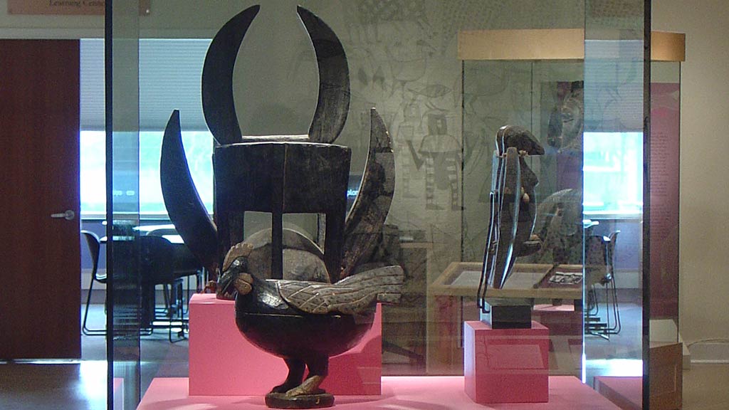 display case image of a black mask with horns behind a black chicken artifact